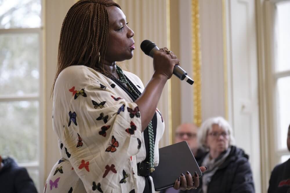 Artist Dzifa Benson speaks into a microphone at an exhibition opening at Orleans House Gallery